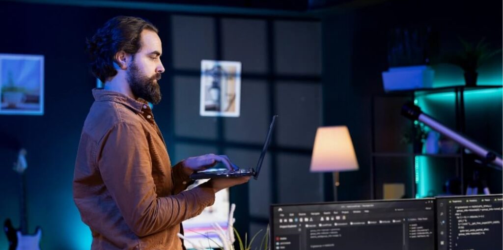 Engineer reviewing code on a laptop in front of monitoring dashboards